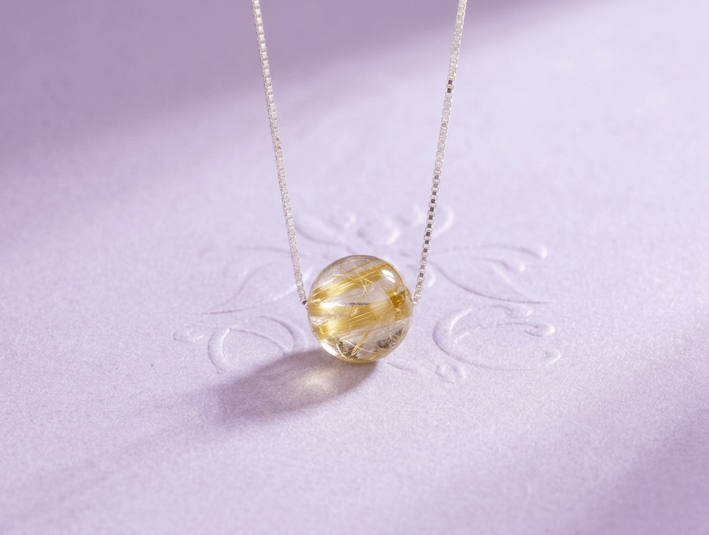 The Natural Golden Rutile Quartz Bead Chain Necklace in Sterling Silver by AME Jewellery is a beautiful piece of jewelry, featuring Venus Hair Stone, a type of transparent Quartz with golden rutile inclusions. These inclusions create stunning patterns that resemble miniature sculptures, making each stone unique and one-of-a-kind.